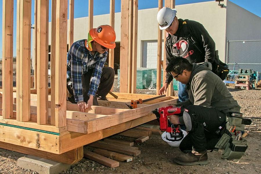 Two San Juan College students with a professor building the frame for a wall